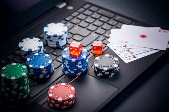 Stacks of poker chips, red dice, and playing cards on a laptop.