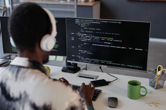 A developer wearing headphones working at a desk with code on a monitor.